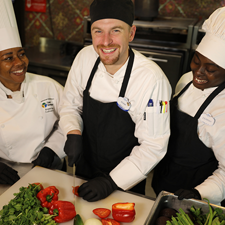Group of three Culinary Team Members, one of whom is prepping brightly colored vegetables