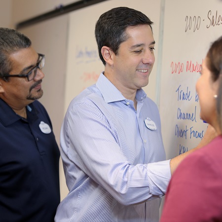 Team member writing on a whiteboard with two other team members looking at him.