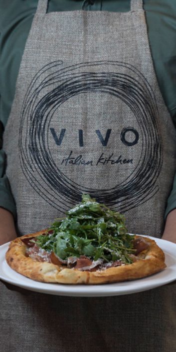 Culinary Team Member at Vivo Italian Kitchen holding a pizza.