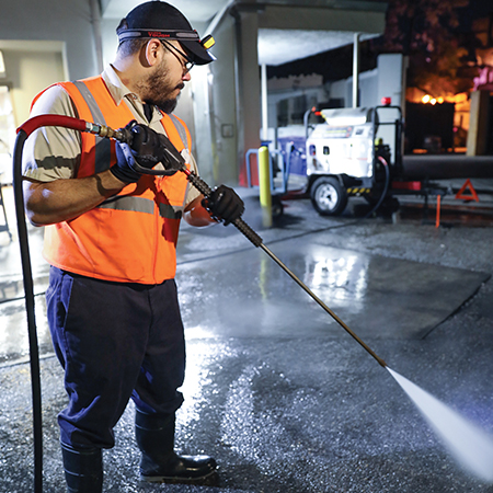 Technical Services Team Member pressure washes the floors inside a theme park maintenance area