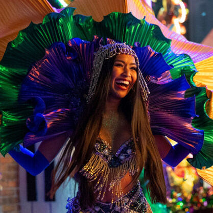 A Mardi Gras performer dressed in green and purple is laughing.