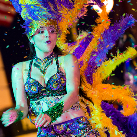 A performer is dancing in the Mardi Gras parade. She is surrounded by confetti.