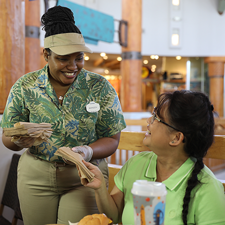 A woman holding napkins is giving napkins to a guest seated at a table.