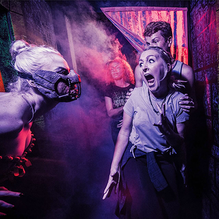 A scareactor scares a woman who is screaming, a man behind her holds her shoulders.