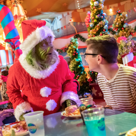 The Grinch and a guest are looking at each other while seated at a table.