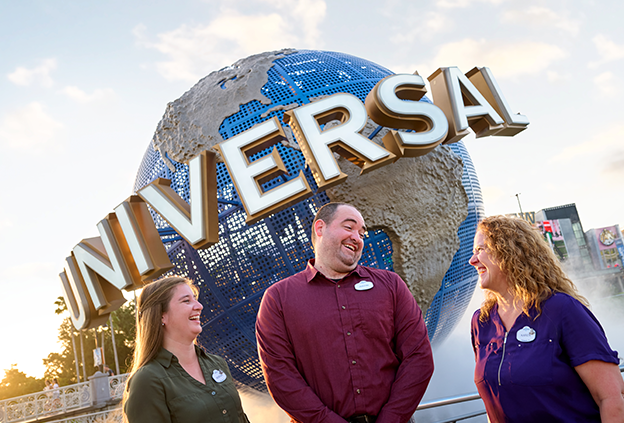 three team members laughing, standing in front of the Universal Globe