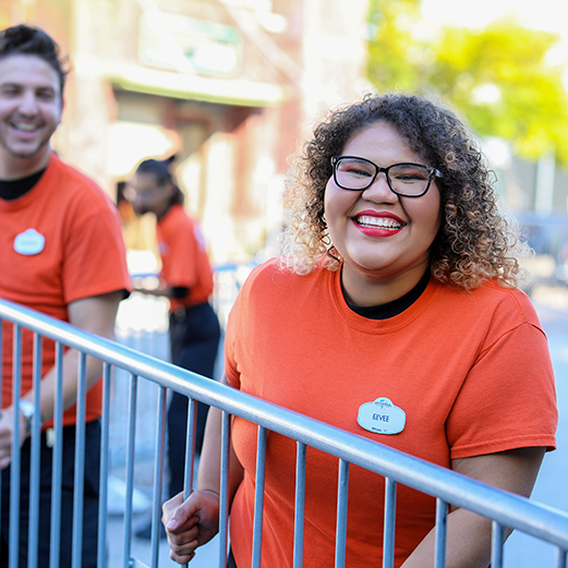 Two Team Members working together to lift and carry a barricade. They are both smiling, the one in front is looking at the camera