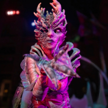 A Halloween performer in an elaborate costume adorned with a striking headpiece, showcasing vibrant colors and intricate designs.