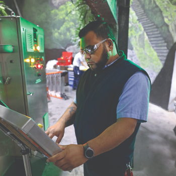 Man wearing protective goggles in a scenic area of an attraction working on a grey control panel