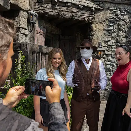 A team Member is taking a photo of two guests posing with The Invisible Man